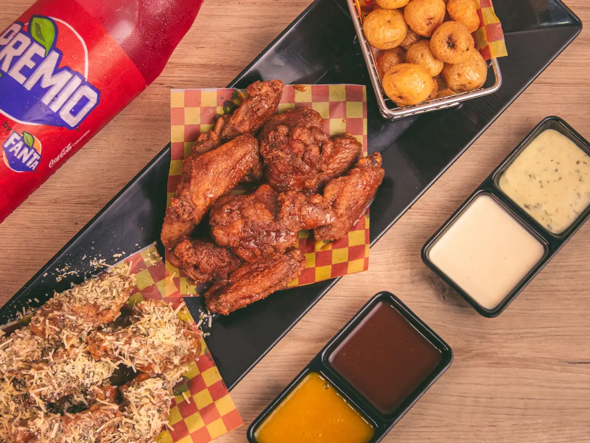 Bandeja de alitas en salsa BBQ y alitas en salsa parmesano, con una canasta de papas criollas, cuatro salsas y una gaseosa de 1,5 litros