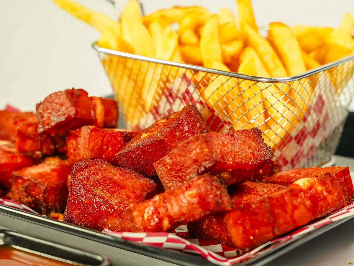 Costillitas de cerdo en salsa roja junto a una canasta de papas a la francesa